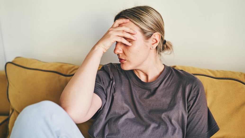 woman holding head in sweat clothes sitting on couch yellow