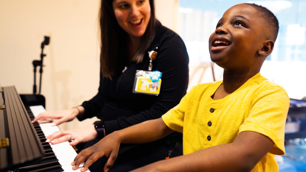 yellow shirt kid looking up very happy wearing playing piano with employee with white shirt 