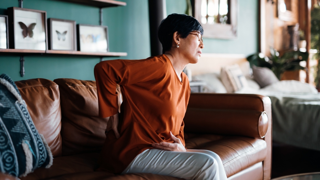 woman holding back in pain sitting on couch