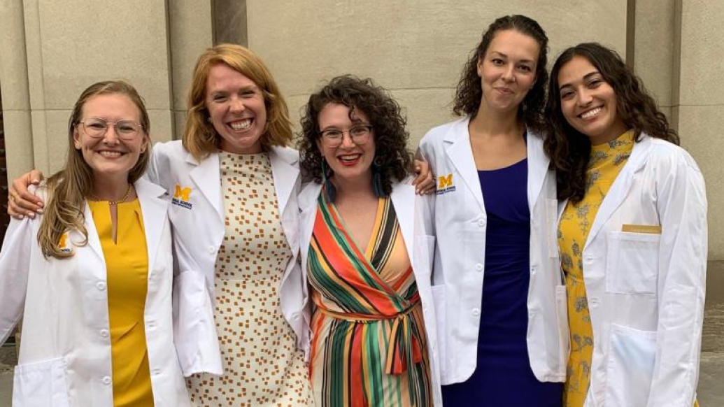 Group of five women wearing white medical coats and smiling