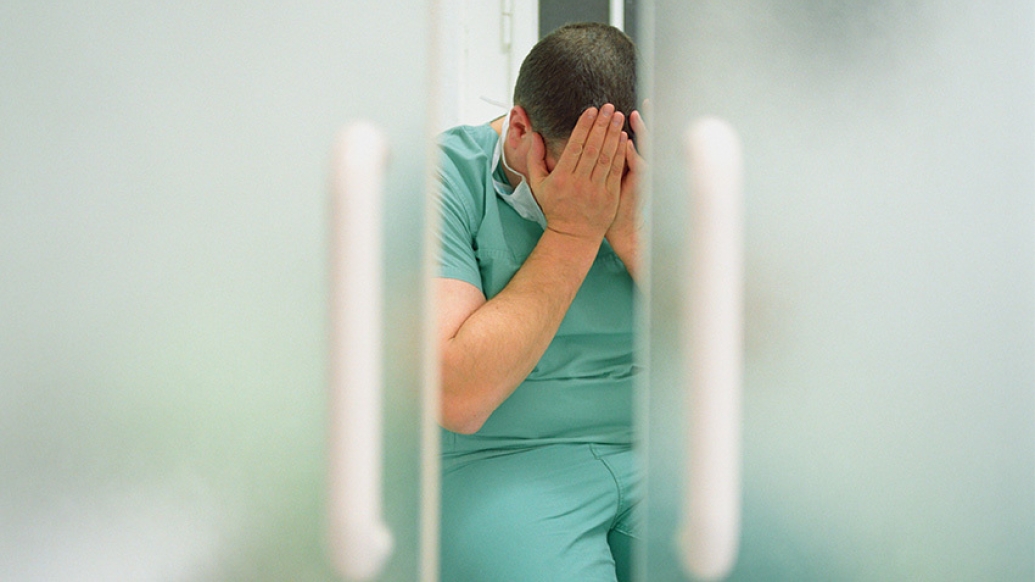 man scrubs holding hands over face sad through door