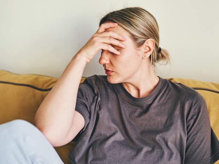 woman holding head in sweat clothes sitting on couch yellow