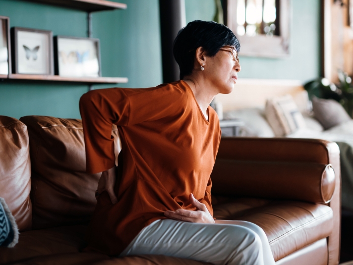 woman holding back in pain sitting on couch