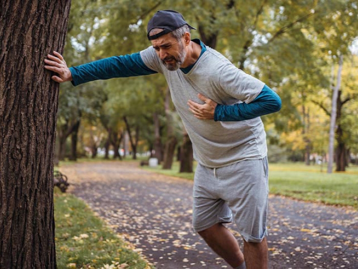 Man leaning against tree by road grabbing his chest