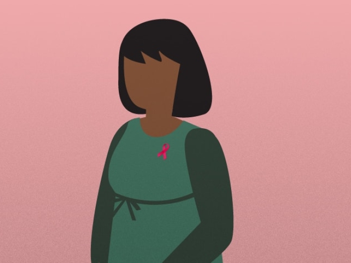 Image of woman wearing green infront of pink background wearing breast cancer pin