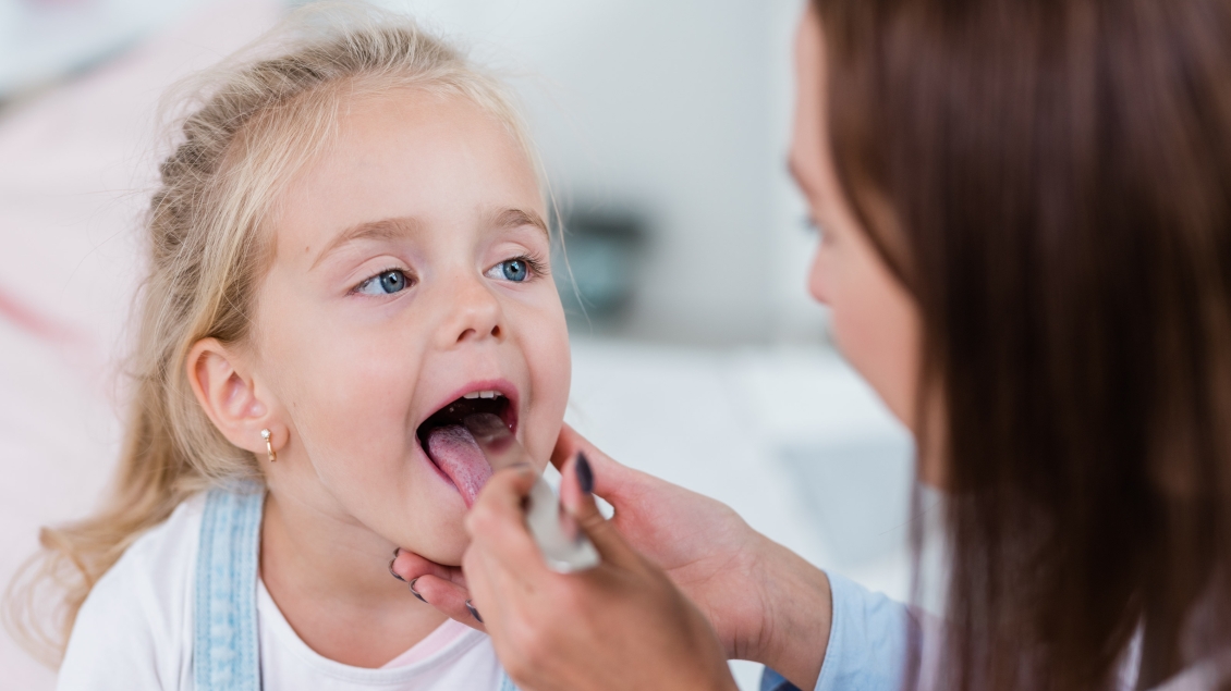 Dermatologist examining little girl's tongue during check-up
