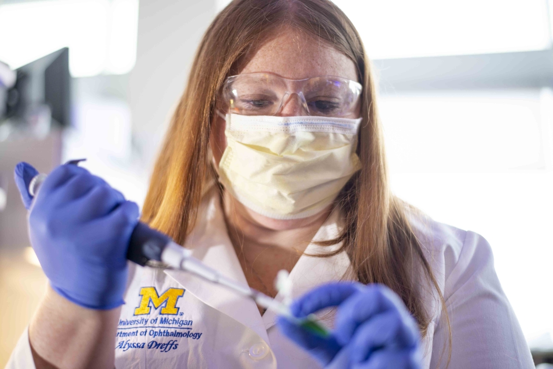 scientist in mask with syringe closer up blue gloves white coat at lab bench