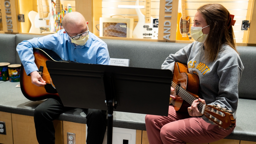 young man holding guitar with blue shirt with employee holding guitar as well both sitting