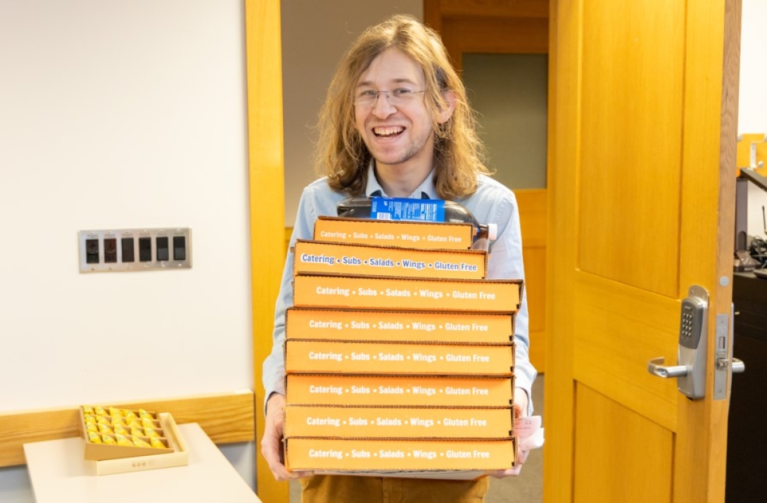 Smiling DCMB student carries pizza boxes into a room