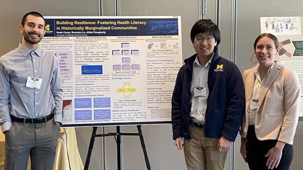 Two men and a woman with name badges standing in front of a research poster display