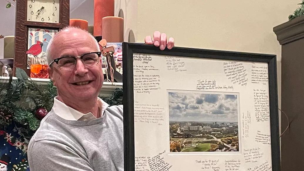 Mike Imperiale smiles holding a signed photo of the campus