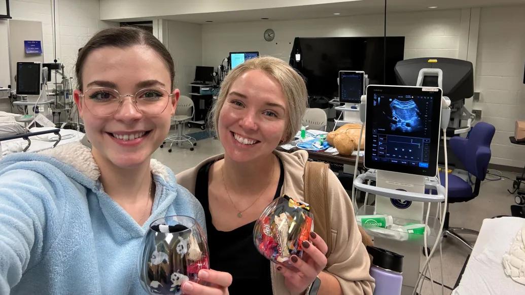 Two medical students stand at the central line and ultrasound guided IV placement station.