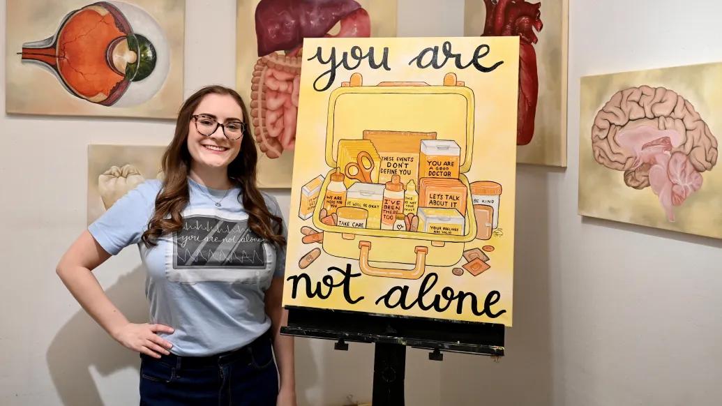 Courtney Burns standing next to the "You Are Not Alone" first aid kit painting by Morgan Graznow. 