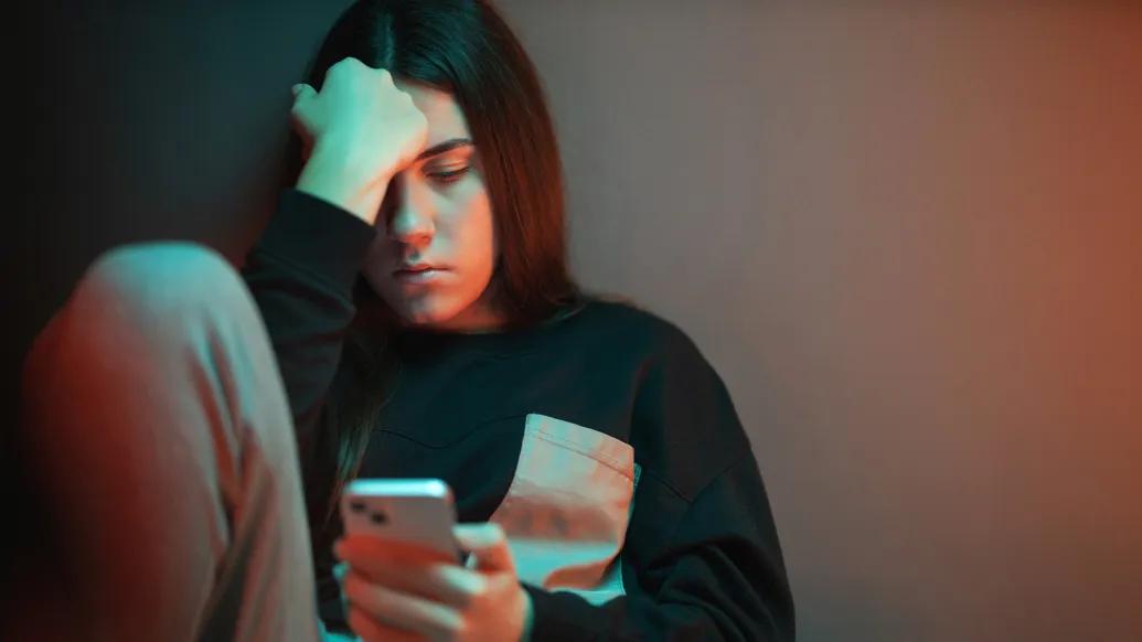 teen looking sad down at her phone dark room 