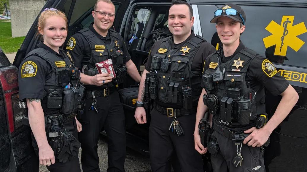 Four police officers standing next to police car. One is holding a bag of blood.