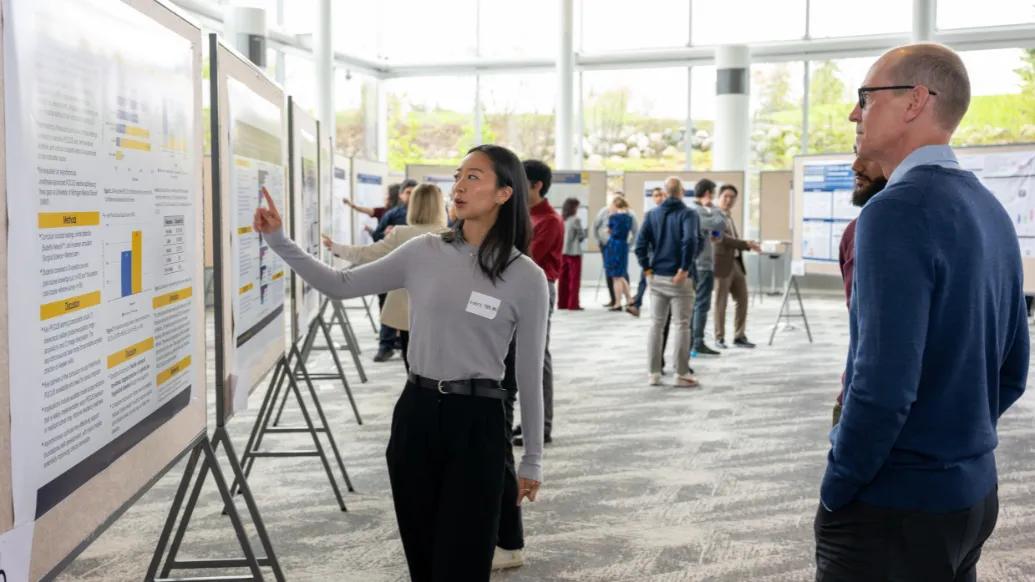 Attendees discuss research posters during the Department of Anesthesiology Research Retreat in a bright atrium at the North Campus Research Complex.