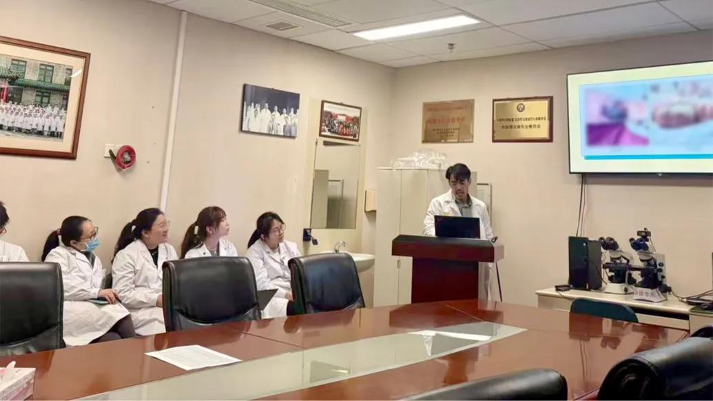 doctor presenting in conference room to other doctors in white coats table in middle and screen 