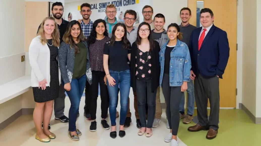 Fourteen people pose together in a hallway outside the University of Michigan Medical School's Clincial Simulation Center.