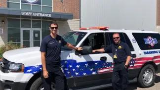 Two emergency services personnel standing in front of an emergency vehicle