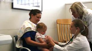 Medical team members using stethoscope for baby held by mother