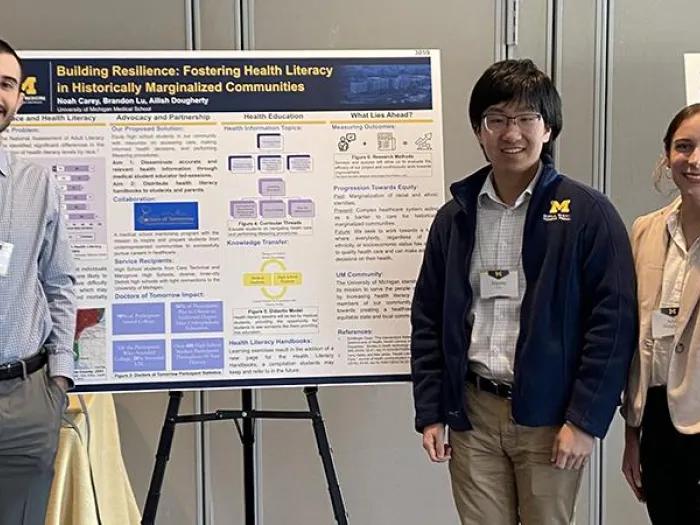 Two men and a woman with name badges standing in front of a research poster display