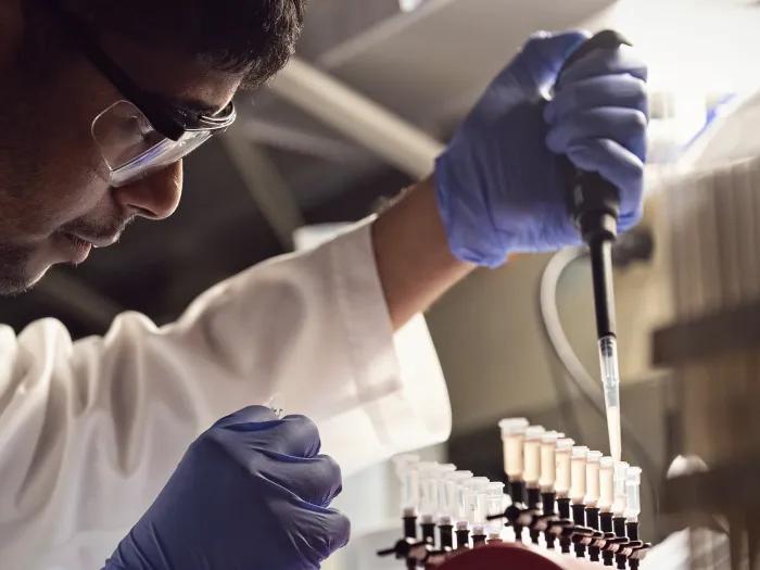 Young brown-skinned male in research lab wearing goggles and blue gloves with test tubes