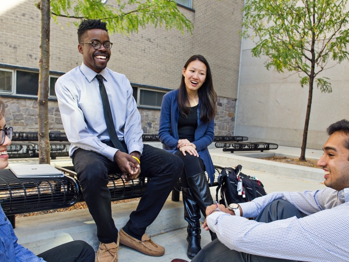 Seated group of diverse students laughing outside campus medical building