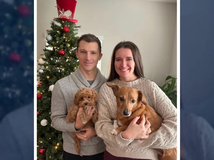 man woman holding brown small dogs christmas photo smiling neutral color sweaters grey biege 
