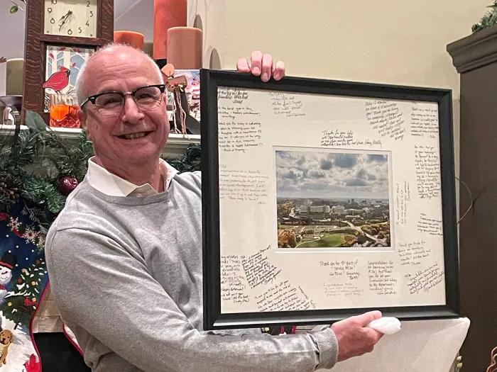 Mike Imperiale smiles holding a signed photo of the campus
