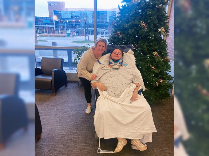 Young man with neck collar in hospital gown poses with his mom in hospital