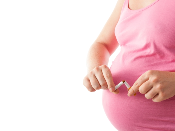 Pregnant woman in pink shirt breaks a cigarette in half in front of her stomach