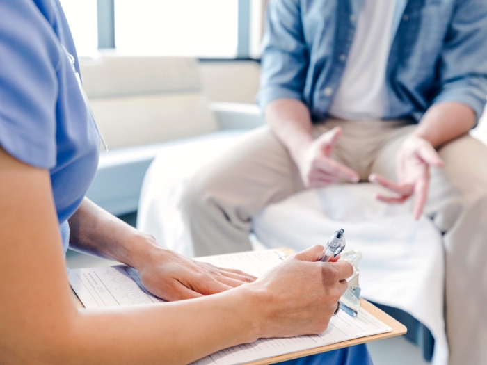 provider sitting writing something down with person in khakis and blue shirt unbuttoned with white shirt under