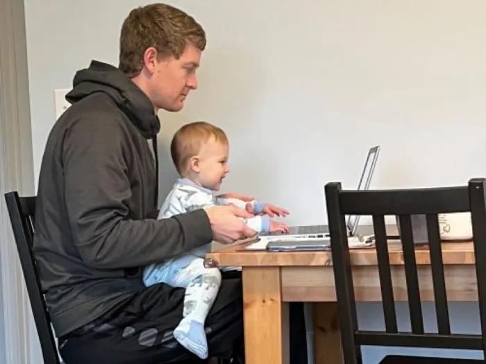 A father with a baby on his lap in front of a laptop