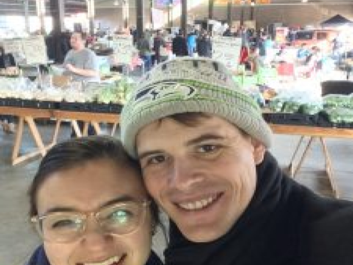 A selfie of a man and a woman standing together with an exhibition/fair in the background