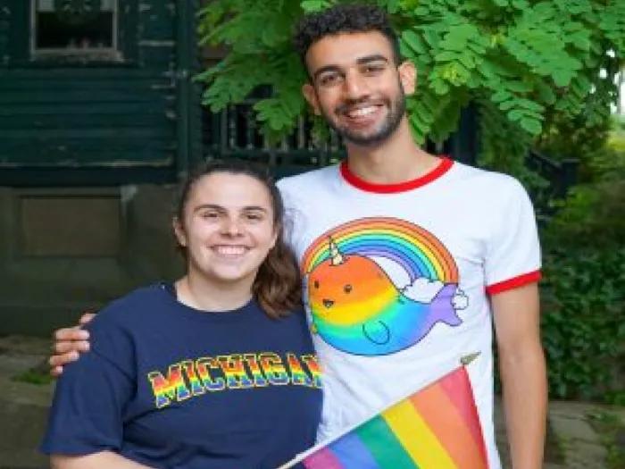 Two people wearing pride shirts and carrying a pride flag