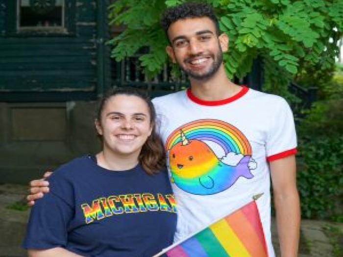 Two people wearing pride shirts and carrying a pride flag