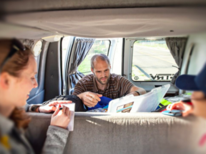 Three people sitting in a van and looking through notes