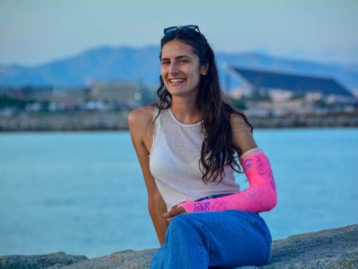 Woman with a pink arm cast sitting at the water's edge