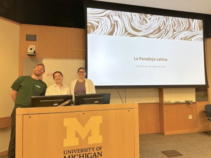 Three people standing at a UM podium in front of a projector screen