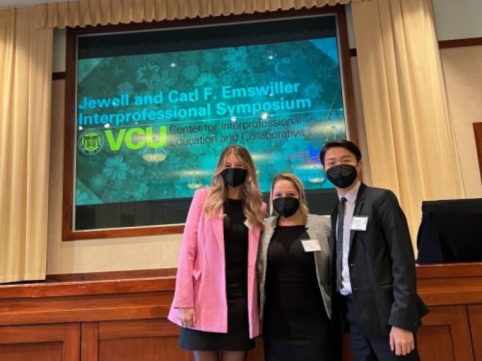 Three people in face masks standing for a photo in front of a projector screen