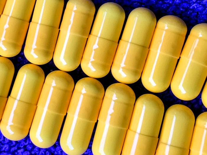 close up photo of yellow pills lined up on a bright blue matt