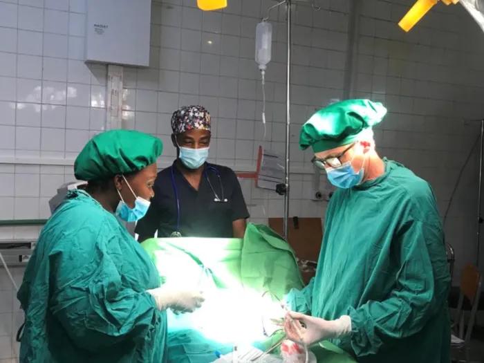 Three people in medical scrubs and surgical masks working on an operating table