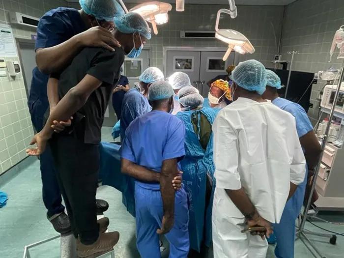Large group of medical students in scrubs and hairnets gathered around the operating table
