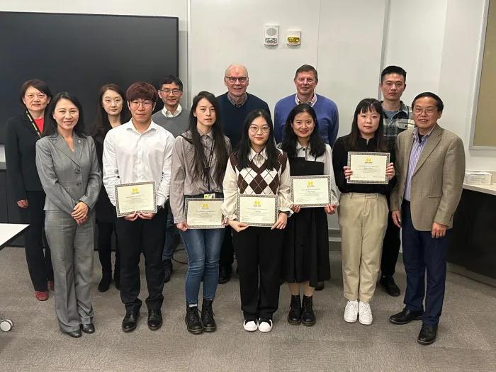 Group of people standing for a photo, some in the front row holding framed certificates