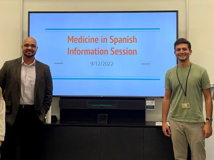 Four people standing on either side of a screen with a presentation slide displayed that reads 'Medicine in Spanish: Information Session"