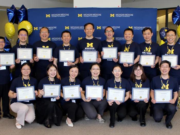 Group of people standing against a blue Michigan Medicine photo wall, holding plaques in their hands