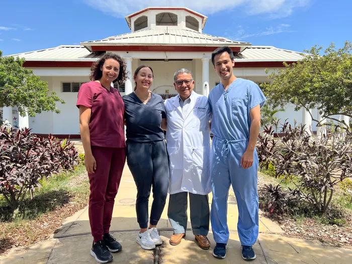 Three medical students in scrubs standing for a photo with a man in a white lab coat