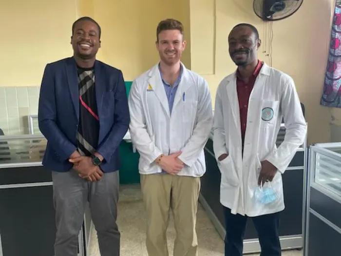 Two men in white lab coats and another man in a dark blazer standing together for a photo
