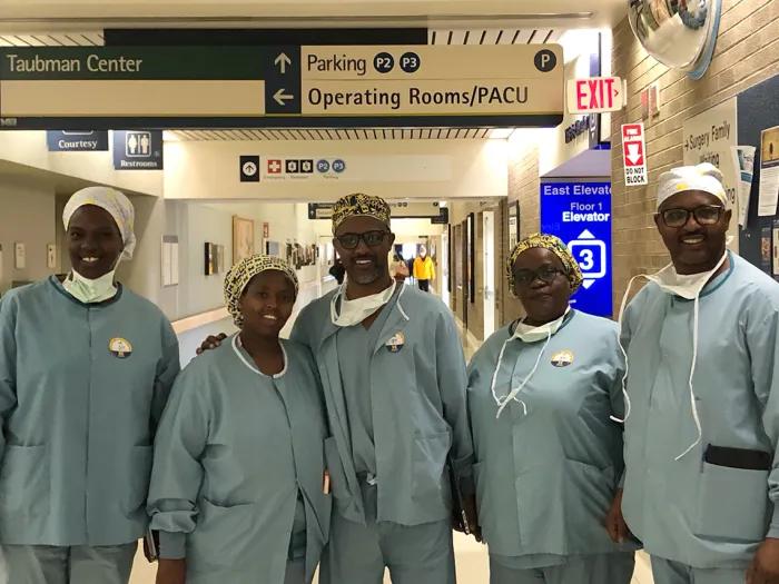 Five people in light blue medical scrubs posing for a photo in a hospital