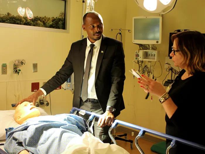 A man and a woman standing next to a hospital bed with a fake dummy lying in it